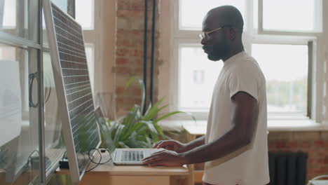 Hombre-De-Negocios-Negro-Cargando-Una-Laptop-Con-Panel-Solar-En-La-Oficina