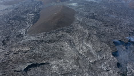 Vast-black-volcanic-lava-Fagradalsfjall-landscape-with-helicopter-in-distance-over-hill.-Aerial-drone-view-of-amazing-volcano-lava-river-scenery,-Iceland,-dolly-in,-day