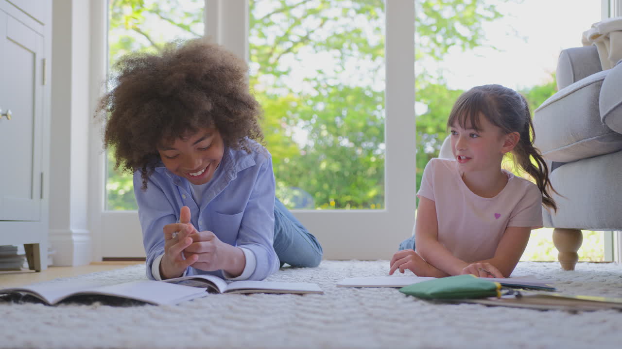 Boy And Girl Lying On Rug In Lounge At Home Doing School Homework Together