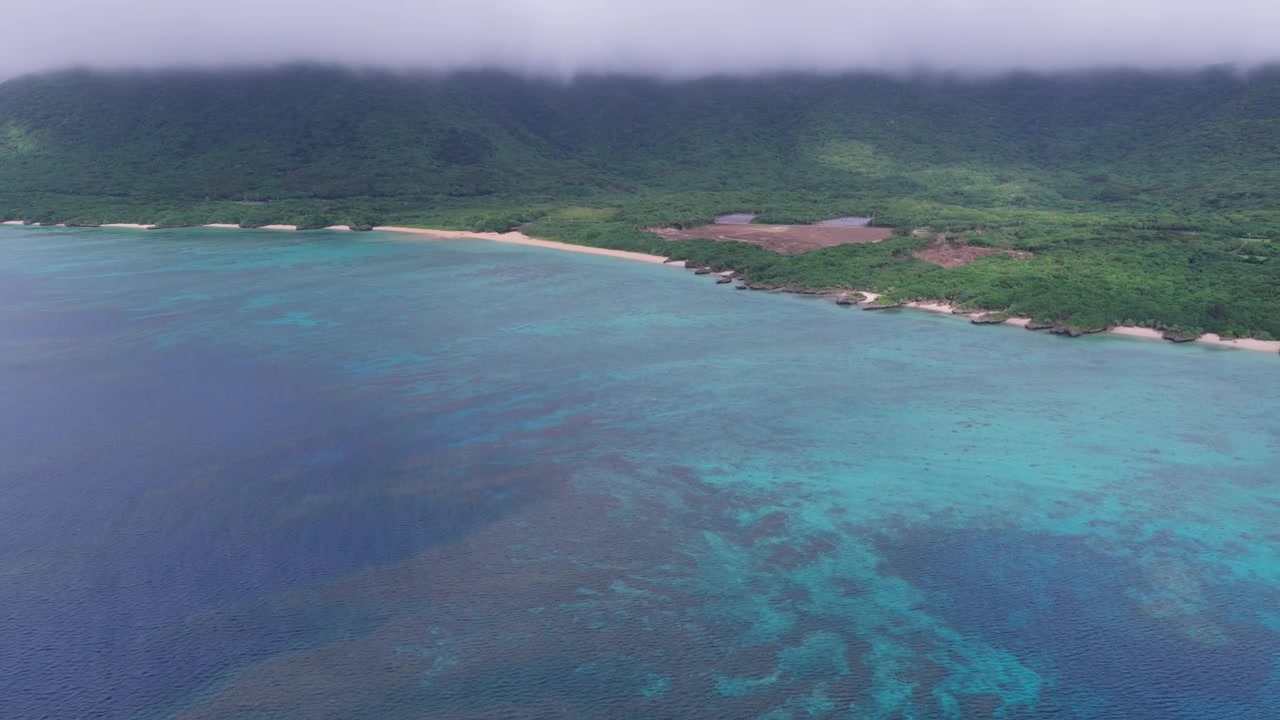 Riprese aeree orizzontali con panoramica a destra e movimento laterale all'indietro a sinistra sopra la costa turchese della spiaggia di Nosokoniaru e della baia di Ibaruma, isola di Ishigaki, Okinawa, Giappone