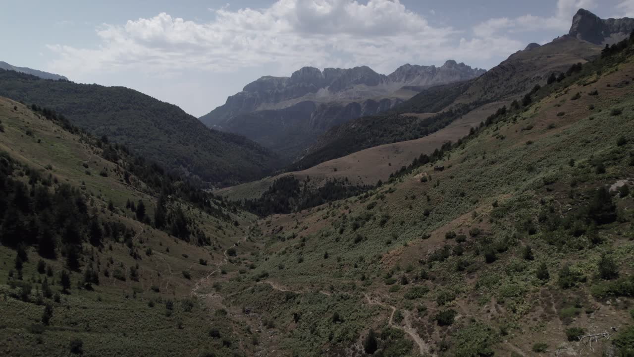4K low-altitude drone shot over the Western Valleys Natural Park in the Aragonese Pyrenees, Spain. A cinematic aerial view of the prairie leading to Ibón de Acherito with mountains in the background.