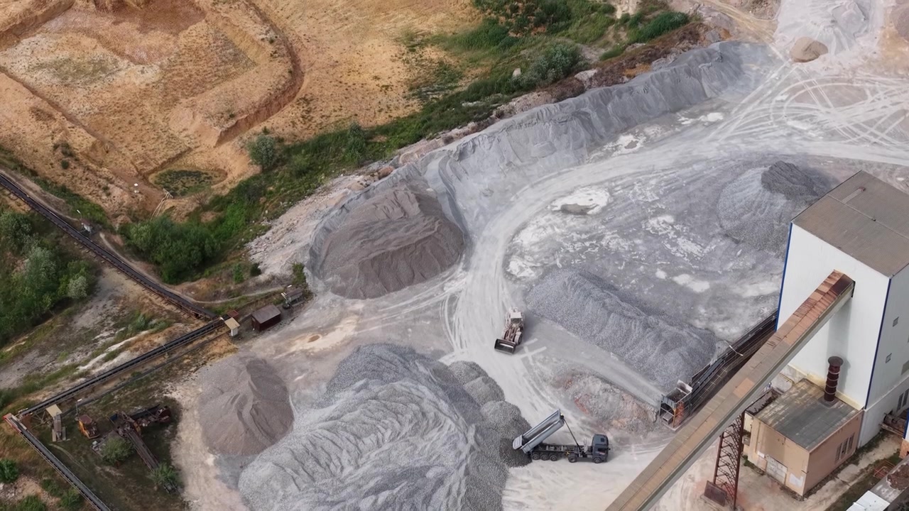 Aerial perspective of a quarry site with trucks, heavy machinery, and an industrial building.