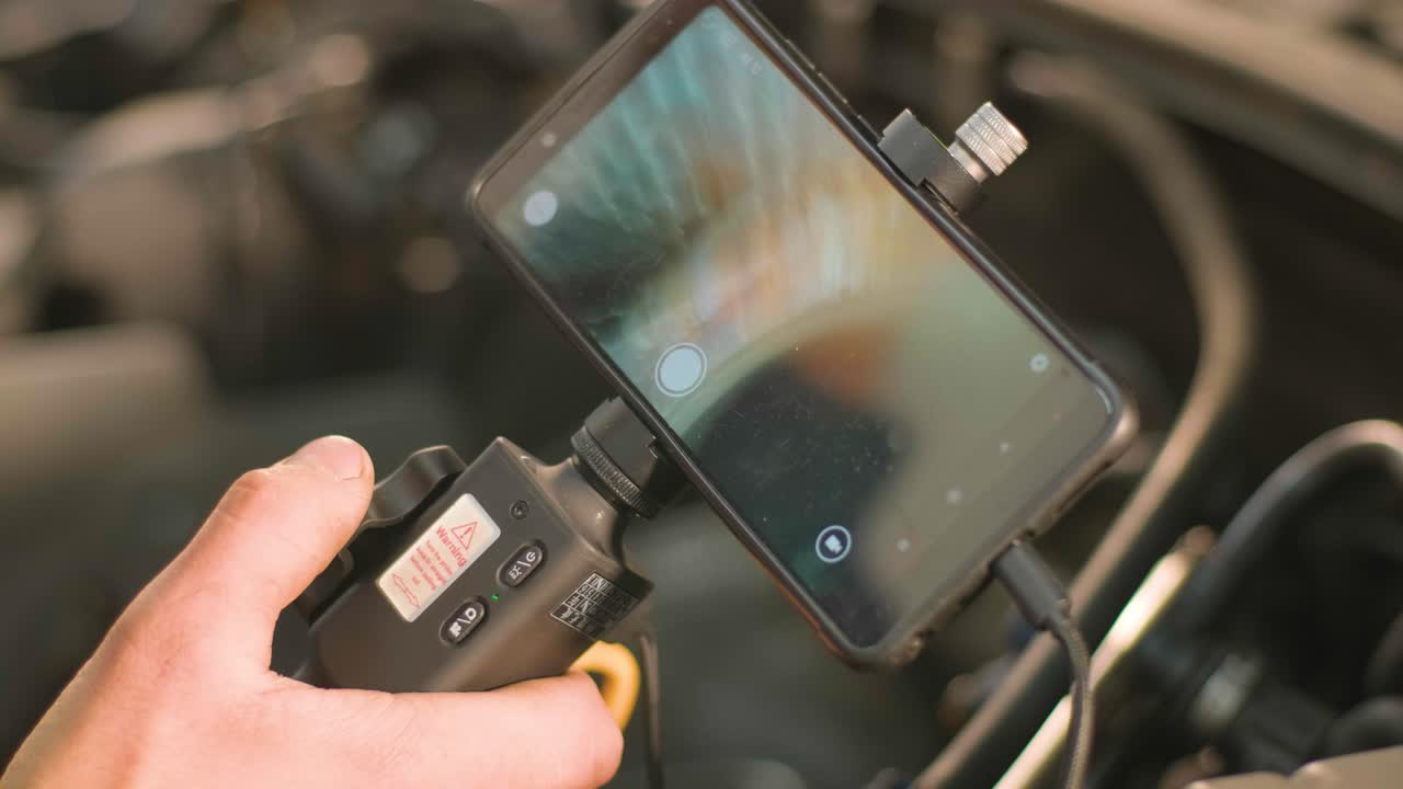 자동차 기계공의 손은 회전 카메라와 휴대 전화로 기술 엔도스코프로 차량 엔진을 확인하고 엔진 헤드와 브를 수리합니다.