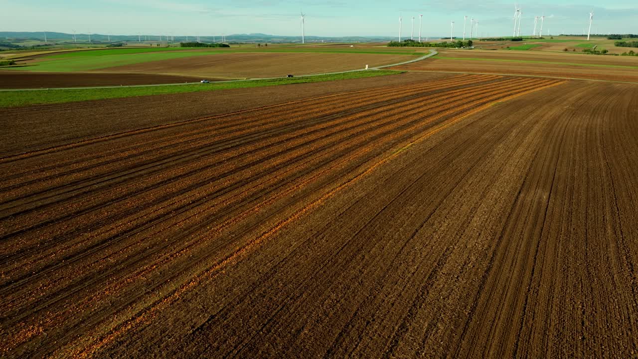 Scenic Aerial View Of A Land During Harvest Season Near Road Overlooking Wind Turbines