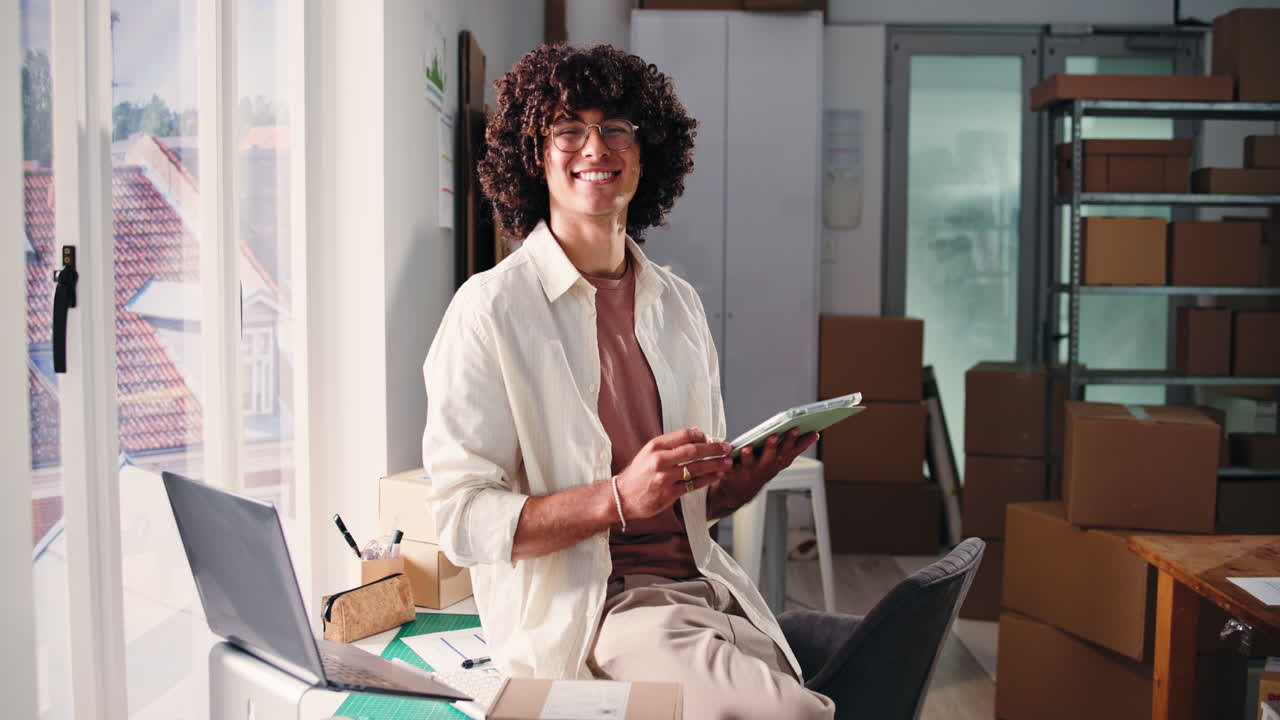 Jeune homme souriant utilisant une tablette dans son bureau de petite entreprise.