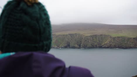 woman in wooly hat looking out over powerful scottish highlands in shetland