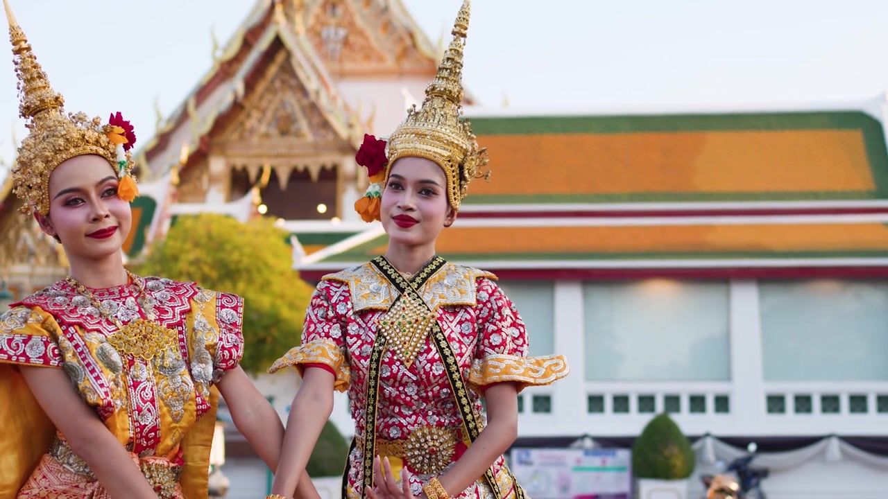 Dos bailarines tailandeses con elaborados trajes dorados realizan movimientos tradicionales fuera de un templo histórico de Bangkok.