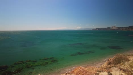 Crimea,-Cape-Megan,-surfers-with-a-sail-cut-through-the-green-water-of-the-Black-Sea-in-warm-spring