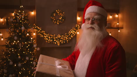 babbo natale tiene tra le mani una grande e bella scatola con un regalo per un bambino ubbidiente per un felice natale. guarda la telecamera e sorride. filmati in 4k di alta qualità