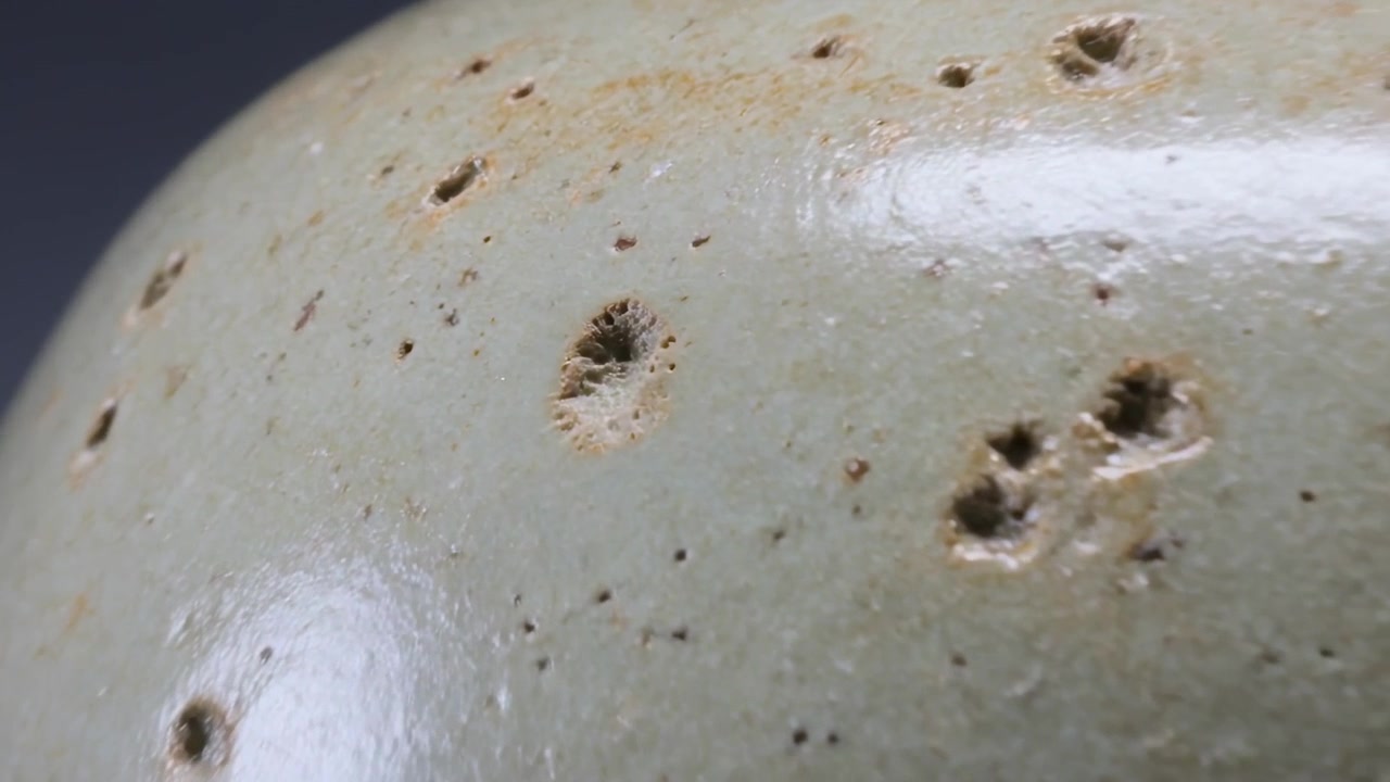 Telecamera in movimento che rivela un vaso smaltato verde pallido su un tavolo da studio, evidenziando le texture porose