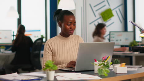 Happy-black-manager-reading-tasks-on-laptop-and-typing-sitting-at-desk