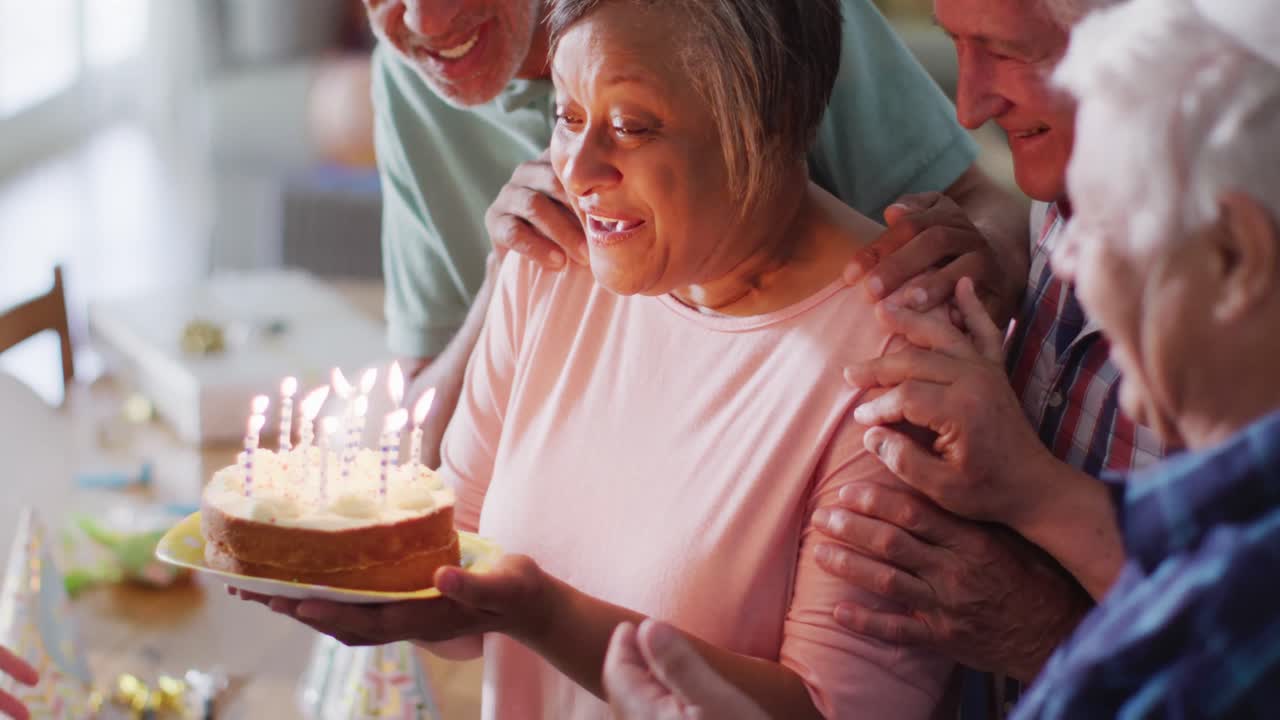Uomo anziano caucasico e felice a una festa di compleanno con torta, insieme ad amici anziani di diverse etnie, al rallentatore.