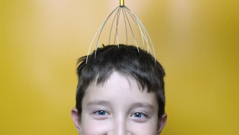 a caucasian boy enjoy head scalp massage by anti stress acupuncture metal octopus tool, equipment, she closes her eyes with pleasure, yellow background, close up view