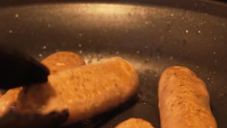 primer plano del chef usando pinzas para girar las salchichas en la sartén caliente