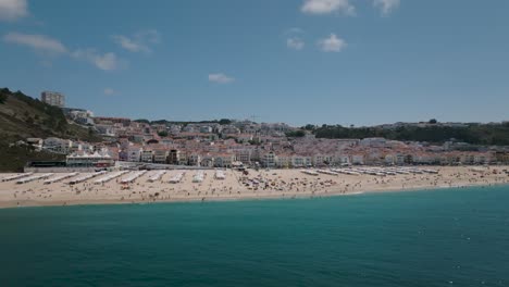 Panorama-Drohnenaufnahme-Des-Strandes-Von-Nazaré-Vom-Meer-Aus-Mit-Einem-Schönen-Blick-Auf-Die-Stadt