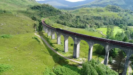 the ancient steam train also known as jacobite, is passing on the old viaduct built in 1900 in the wonderful glenfinnan valley in scotland.