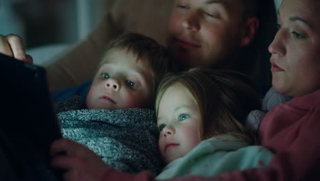 happy family using tablet computer with children mother and father enjoying watching entertainment with kids on touchscreen technology relaxing before bedtime