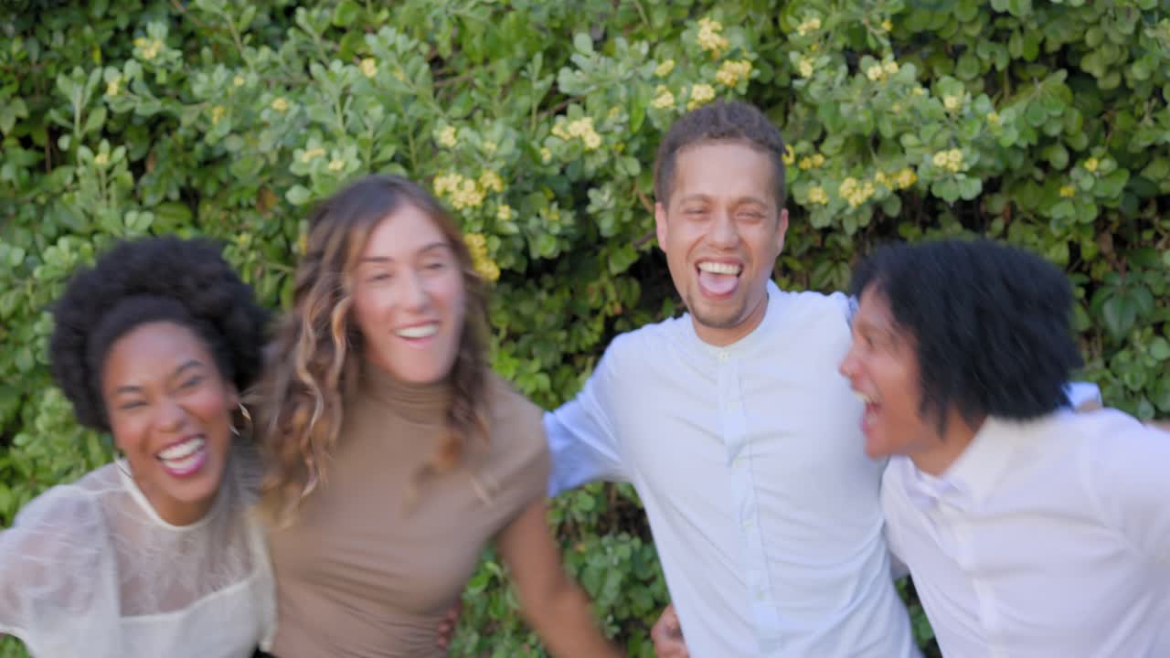 Amigos diversos posando para la cámara junto a un seto, una mujer tira de un hombre hacia adelante mientras otros se apresuran entrelazando los brazos.