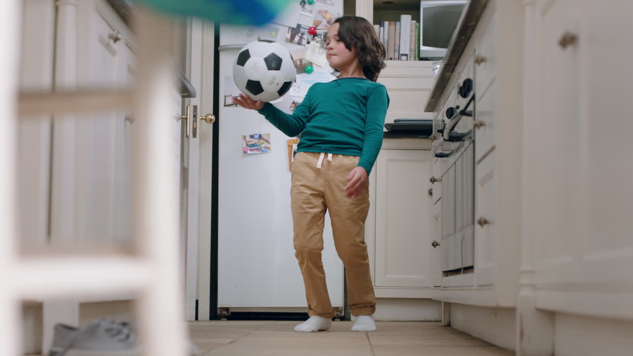niño feliz jugando con una pelota de fútbol en la cocina practicando habilidades divirtiéndose en casa el fin de semana