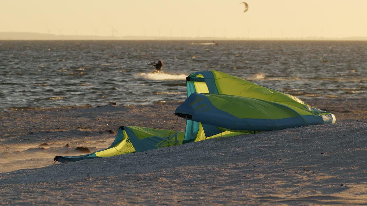 cometa de kitesurf amarillo acostado en la playa, ondeando en el viento fuerte durante la hora dorada del atardecer