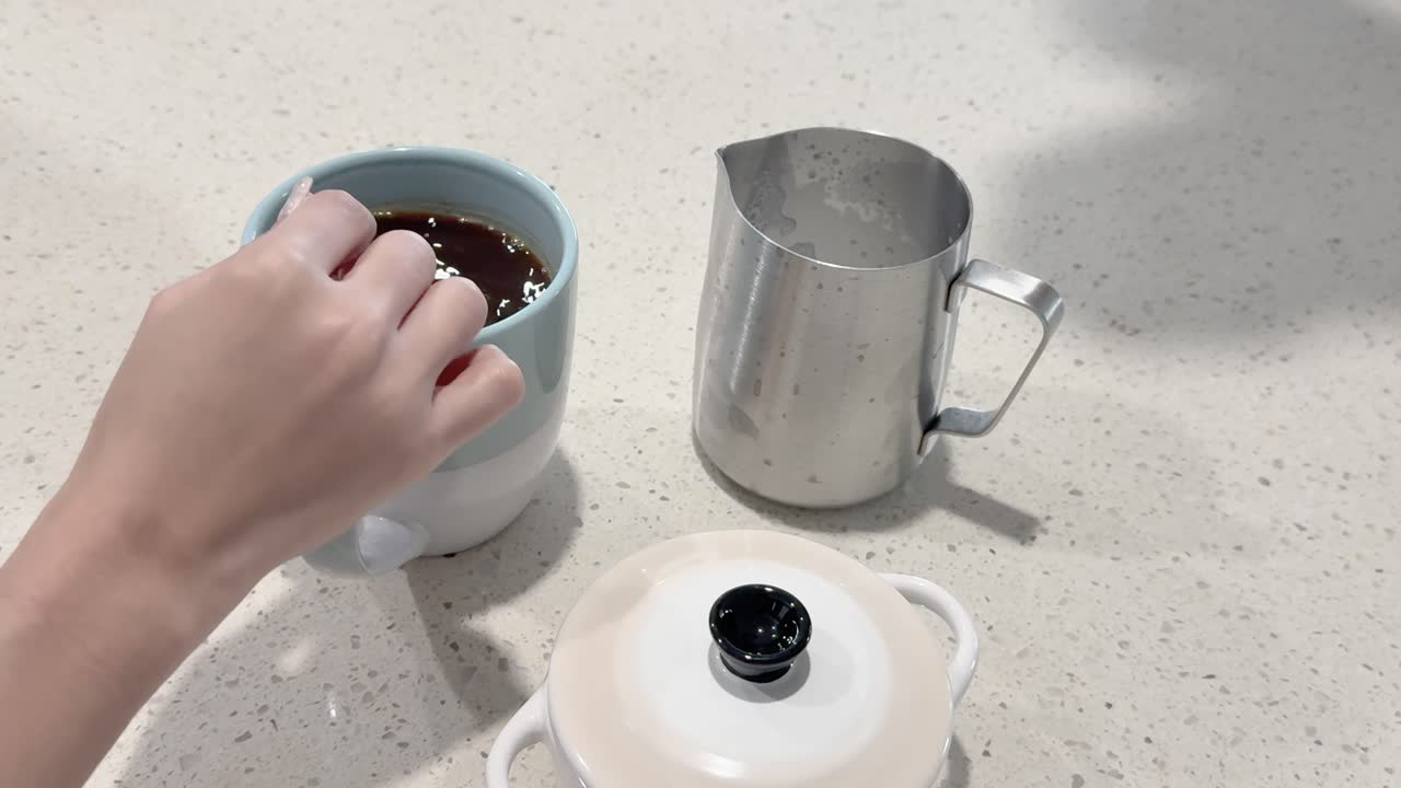 A hand stirs sugar into a coffee cup using a spoon on a kitchen counter