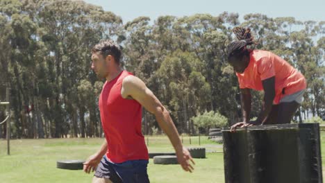 Two-diverse-fit-men-climbing-over-fences-and-running-on-obstacle-course-in-the-sun