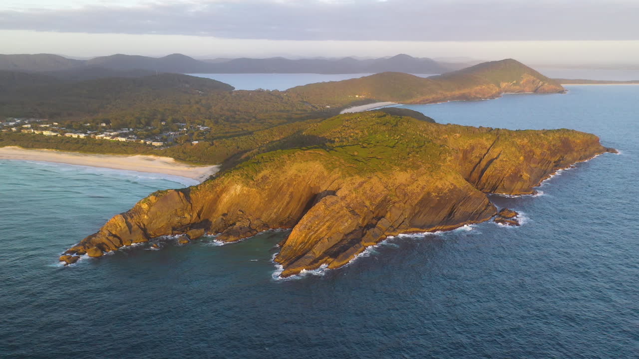 Ripresa aerea di una città costiera del Nuovo Galles del Sud e scogliere a picco al tramonto.