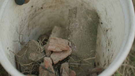 handheld close up shot of throwing old bricks into a bucket filled with more bricks