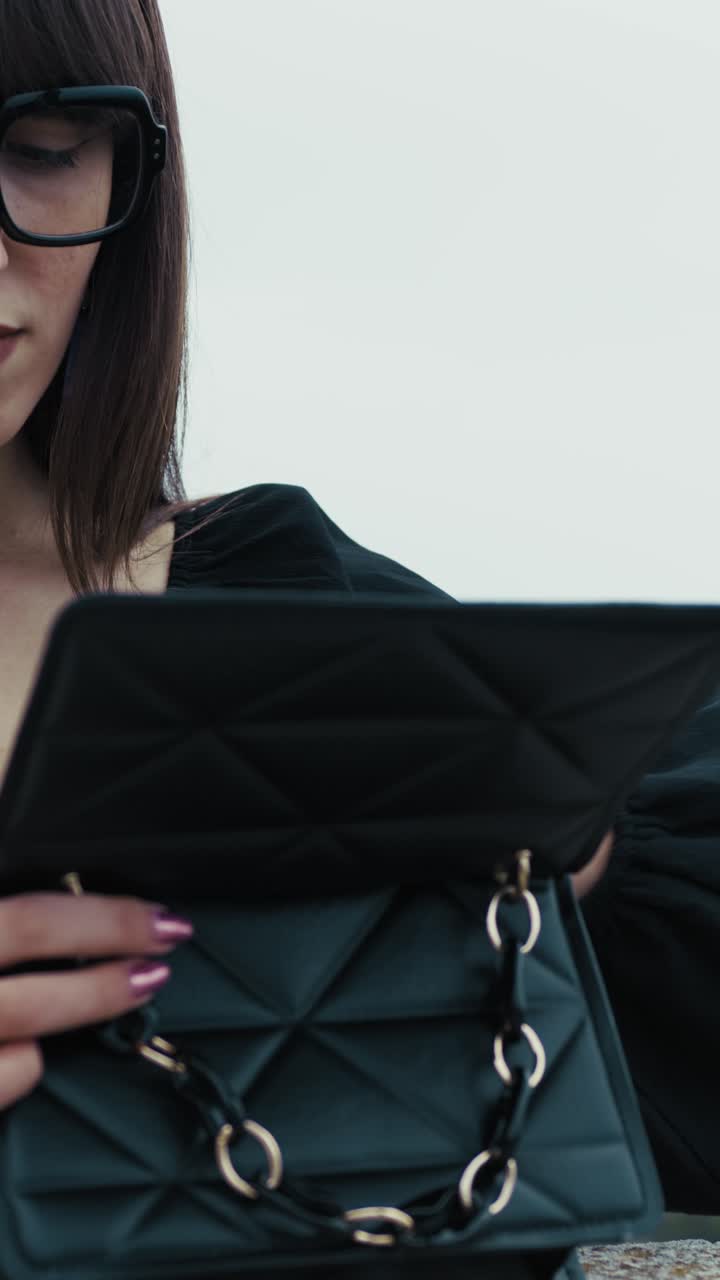 Donna all'aperto che cerca qualcosa nella sua borsa nera