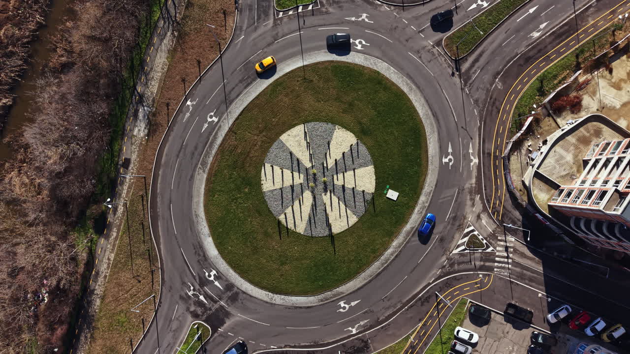 Roundabout with stone art design located in a busy city area during daytime with cars moving around and parked vehicles nearby