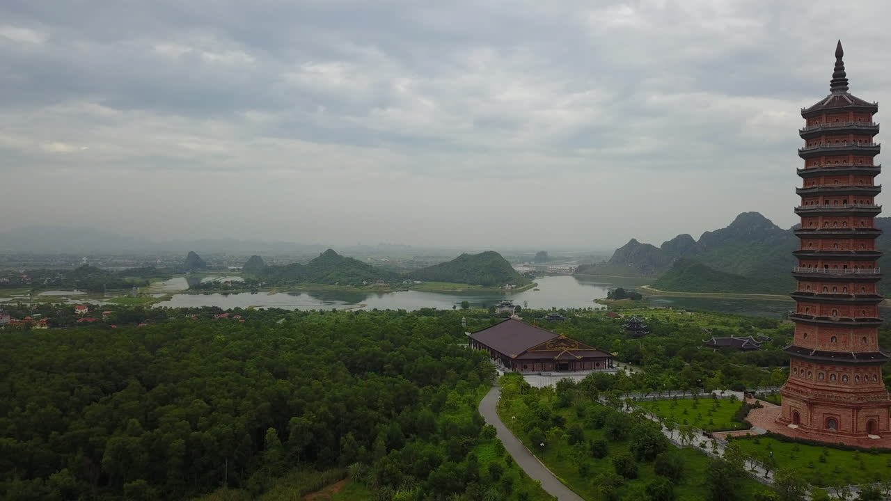 A zoom-out aerial view of the magnificent Bái Đính Pagoda in Ninh Binh, Vietnam, on a cloudy day. Showcases the impressive scale of the Buddhist temple complex within the surrounding landscape.