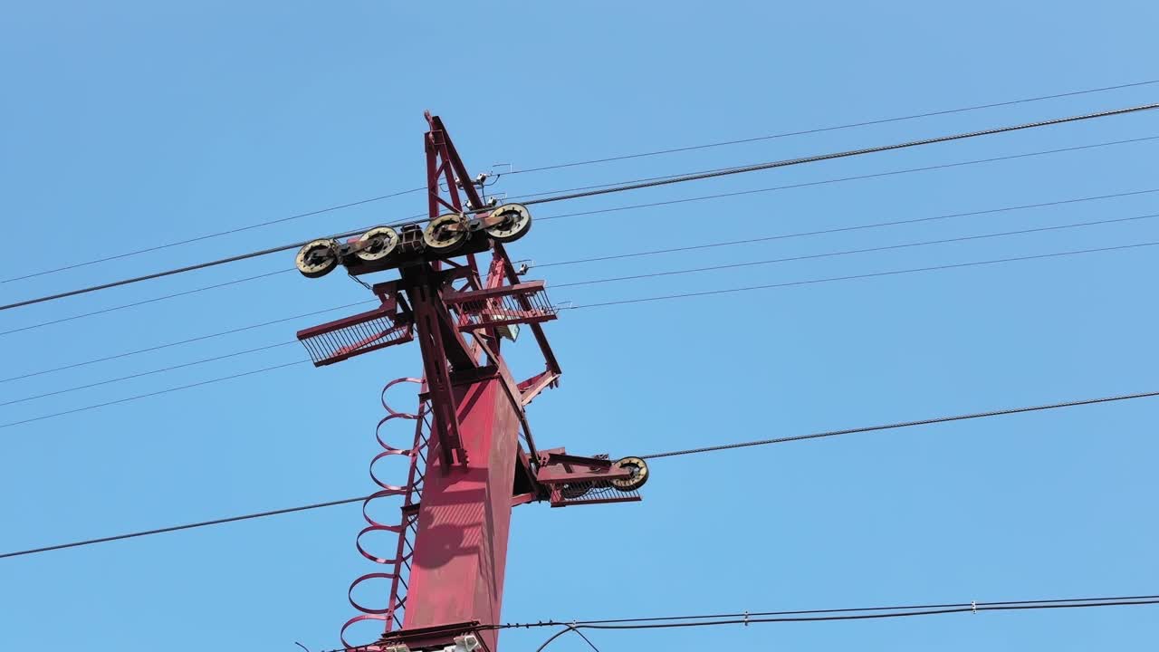 Statisk optagelse af et tovbanetårn med roterende hjul og spændte stålkabler mod en klar blå himmel, der fremviser transportinfrastruktur og mekanisk design!!
