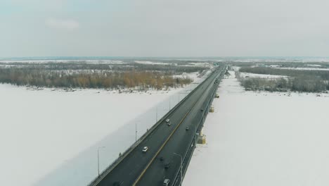 cars-drive-along-gray-bridge-making-shadow-on-frozen-river