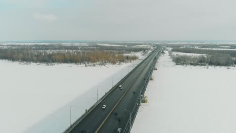 los coches circulan a lo largo del puente gris haciendo sombra sobre el río congelado