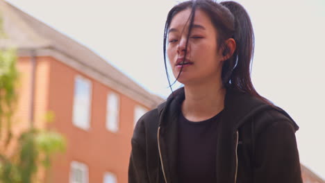 Close-Up-Of-Young-Woman-Exercising-On-Urban-Street-Wearing-Wireless-Earbuds-Checking-Smart-Watch-Before-Run