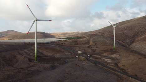 aerial shot in orbit of two wind turbines and a greenhouse in the background