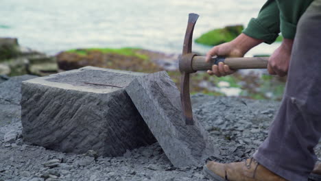 handheld shot of a cancagua stone craftsman picking at a slab of stone on the shoreline of ancud on chiloe island, bright daylight