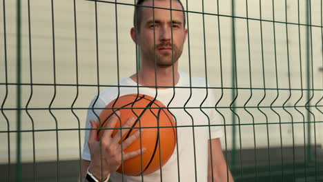 man holding basketball behind a fence