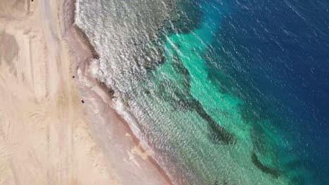 Ojo-De-Pájaro-Aéreo-Descendiendo-Sobre-Una-Playa-Desierta-Con-Aguas-Turquesas,-Tabuk