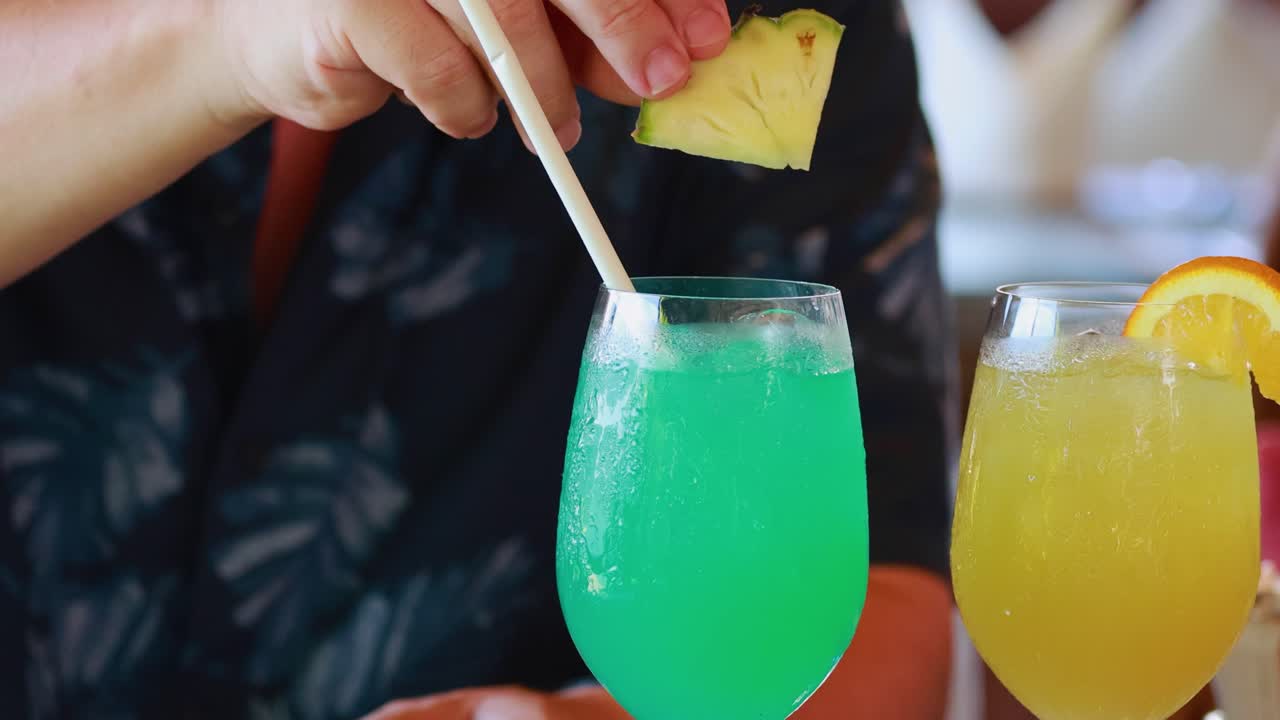 A bartender stirs vibrant cocktails with garnishes in a lively Phuket bar setting