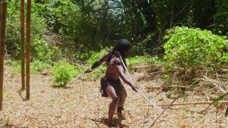 in a forest setting, a dark-skinned, muscular guy embodies tarzan in his costume.