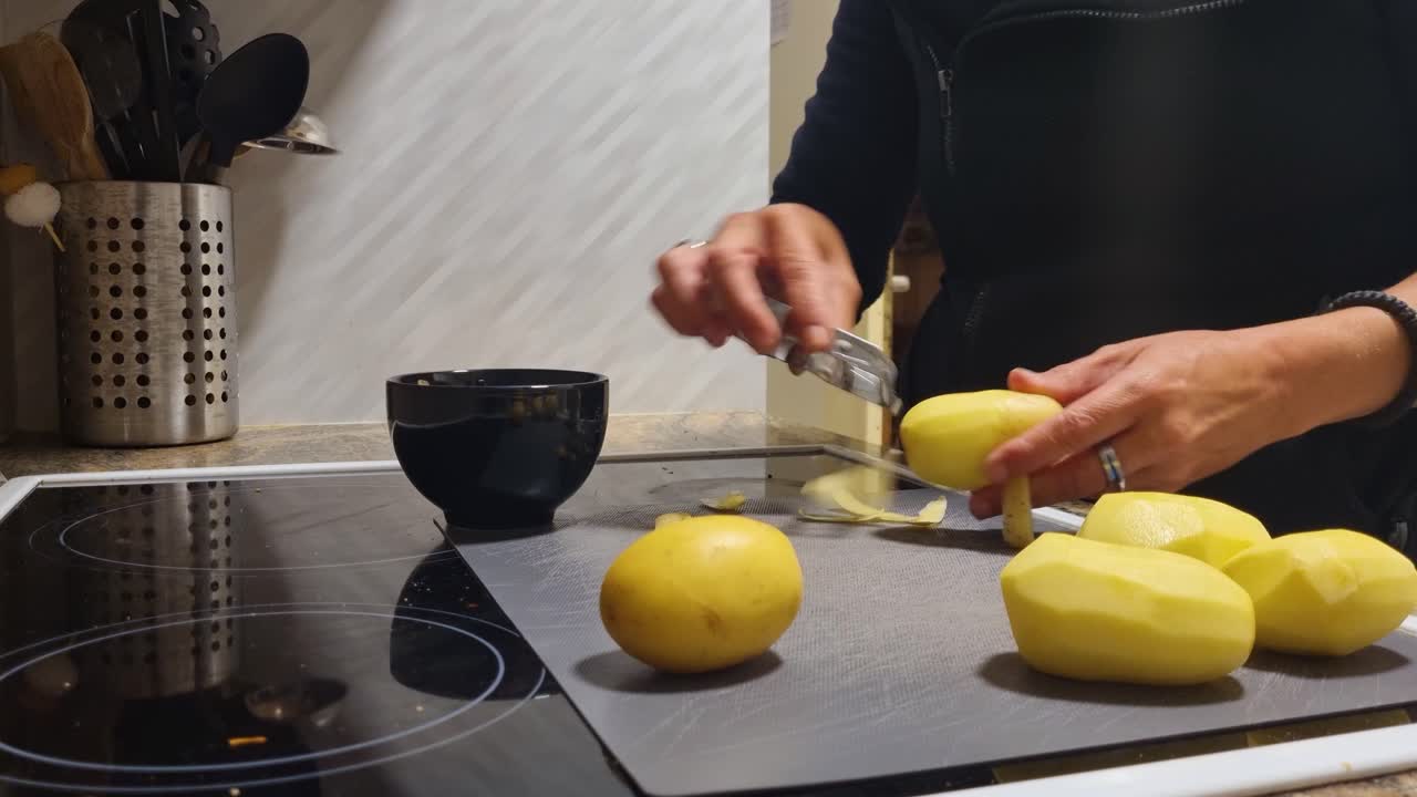 Primer plano de una mujer pelando patatas en su cocina europea, preparando ingredientes para una comida tradicional suiza casera