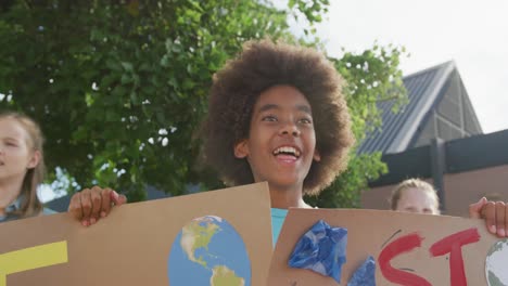 video portrait of happy african american schoolboy holding protest placards and chanting outdoors