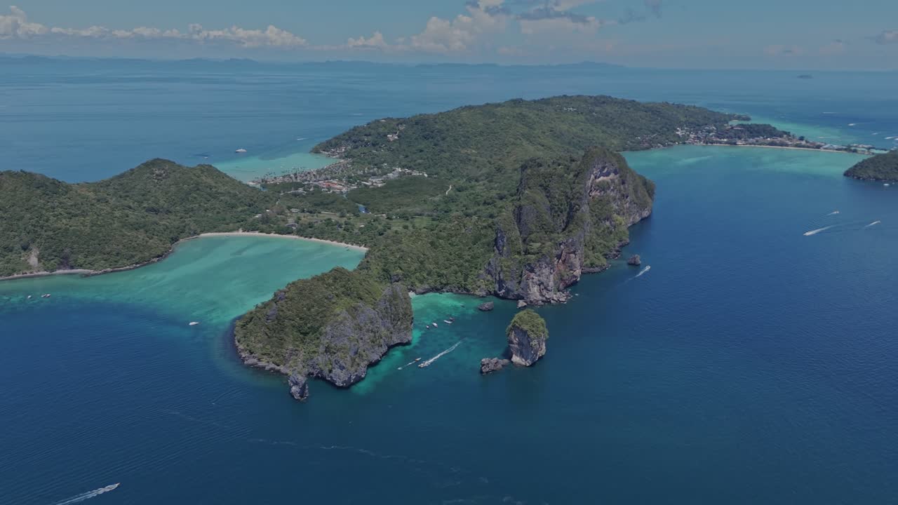 Aerial semi orbit around a dramatic limestone outcrop rising from deep blue ocean under cloudless skies on a sunny April day in Phi Phi Islands, Thailand.