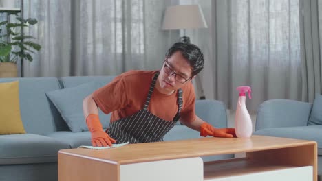 un ama de casa asiático enojado con un delantal limpiando la mesa con el spray en casa