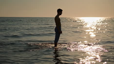 man standing in the ocean at sunset