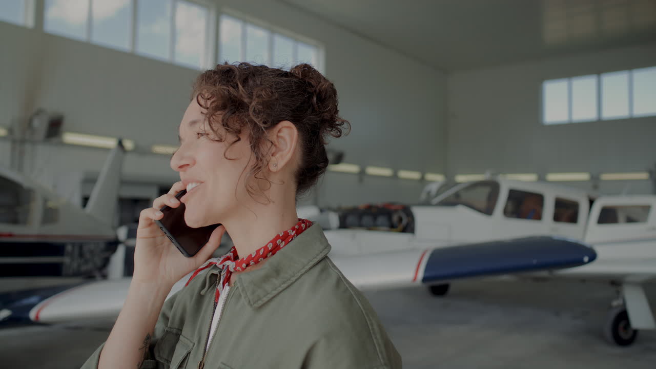 Smiling Female Ground Crew Member Having Phone Conversation in Aircraft Hangar