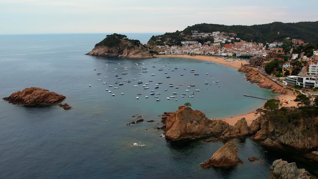 Pemandangan udara menakjubkan Tossa Del Mar di Spanyol, bergerak menyamping di atas kota dan tepi laut, menyingkap teluk, perahu layar, dan pemandangan kota tepi laut yang indah.