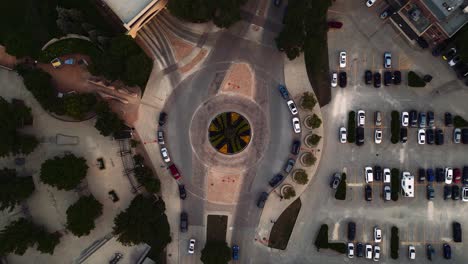 long 4k clip aerial drone rising on decorative garden pavement city infrastructure cars traffic cobblestone roundabout roadway urban downtown city street route intersection junction parking lot