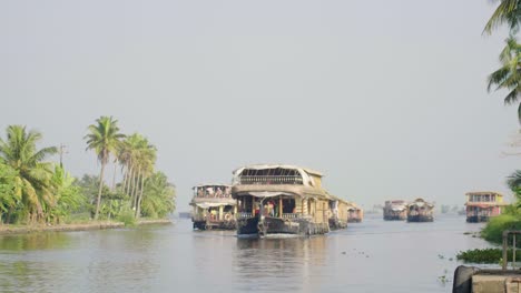 a group of houseboats approaches the cameraman in the kerala backwaters slowly during the midday sun